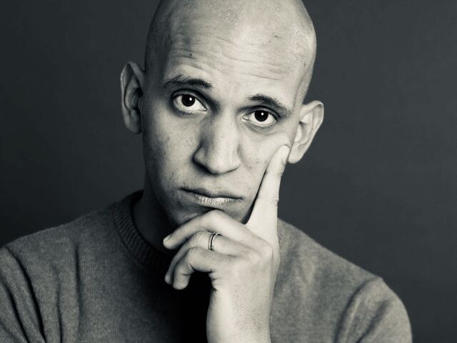 Zwart-wit portret van een man met een kaal hoofd, die nadenkend met zijn hand op zijn kin leunt.