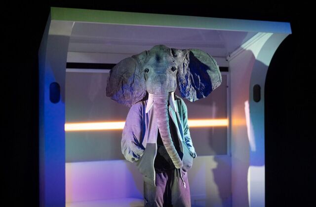 Een olifant in een kostuum staat in een futuristische setting met kleurrijke verlichting.