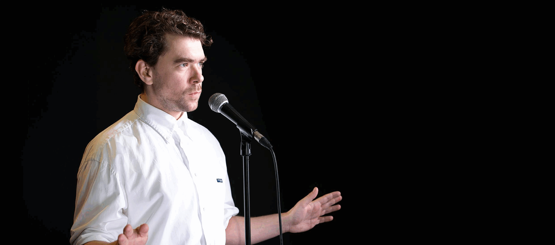Man met een microphone die een presentatie geeft, met een zwarte achtergrond.