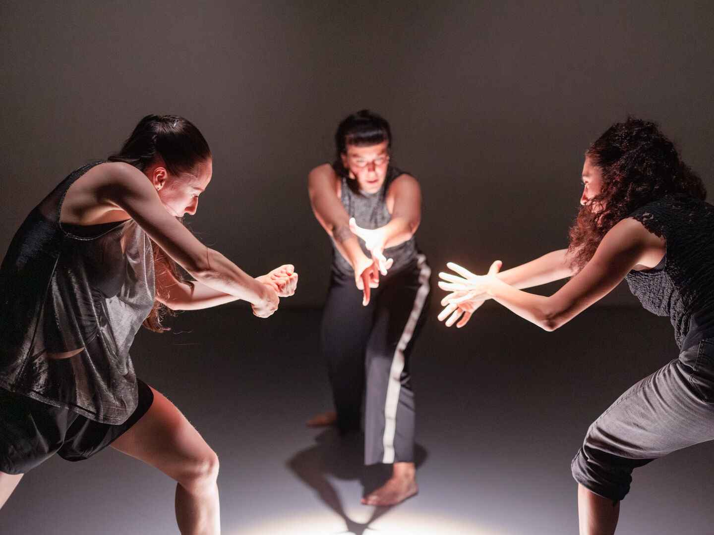 Drie dansers in dynamische pose, interactief met elkaar in een geïntensiveerde choreografie op een lichte vloer.