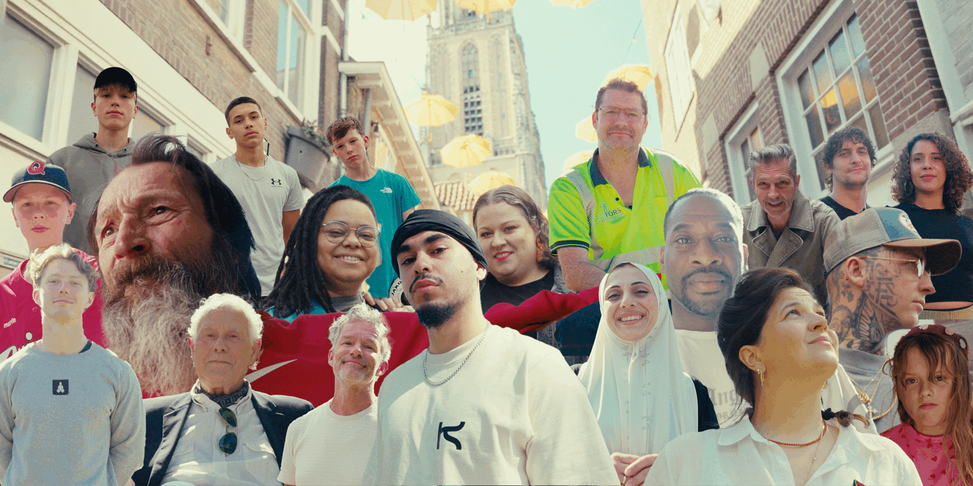 Een diverse groep mensen poseert samen op een straat, met een heldere lucht op de achtergrond.