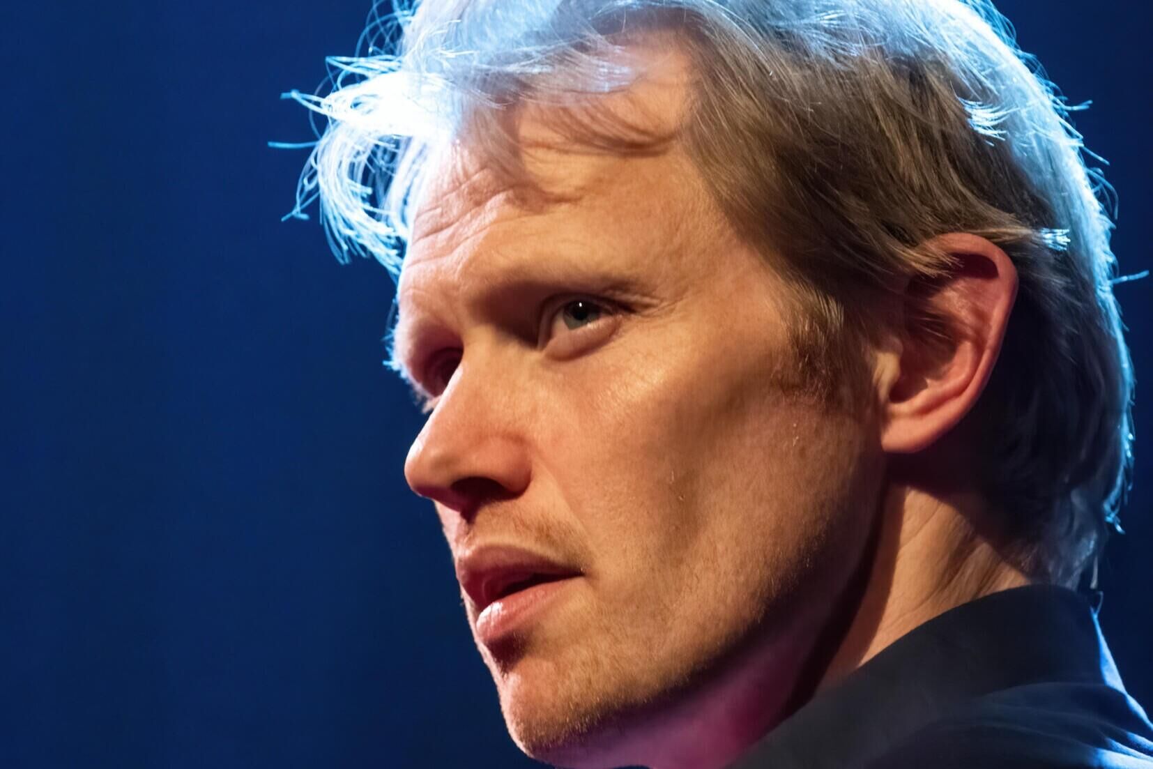 Portret van een man met een lichte huid en blond haar, die in profiel staat met een serieuze uitdrukking.