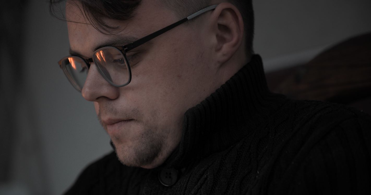 Een man met een bril kijkt geconcentreerd naar beneden, in een sfeervol verlichte omgeving.