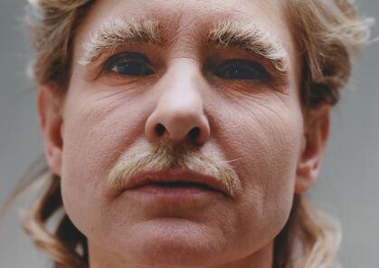 Een close-up portret van een persoon met een lichte baard en opvallende wenkbrauwen, met een neutrale gezichtsuitdrukking.
