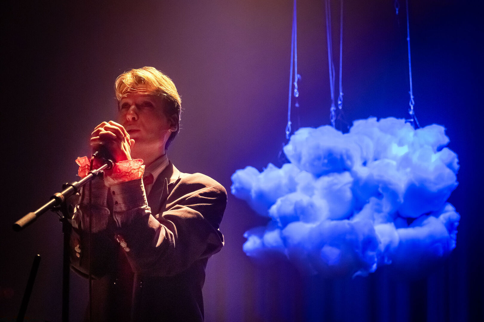 Een performer staat bij een microfoon, omringd door een hangende, verlichte wolk van katoen.