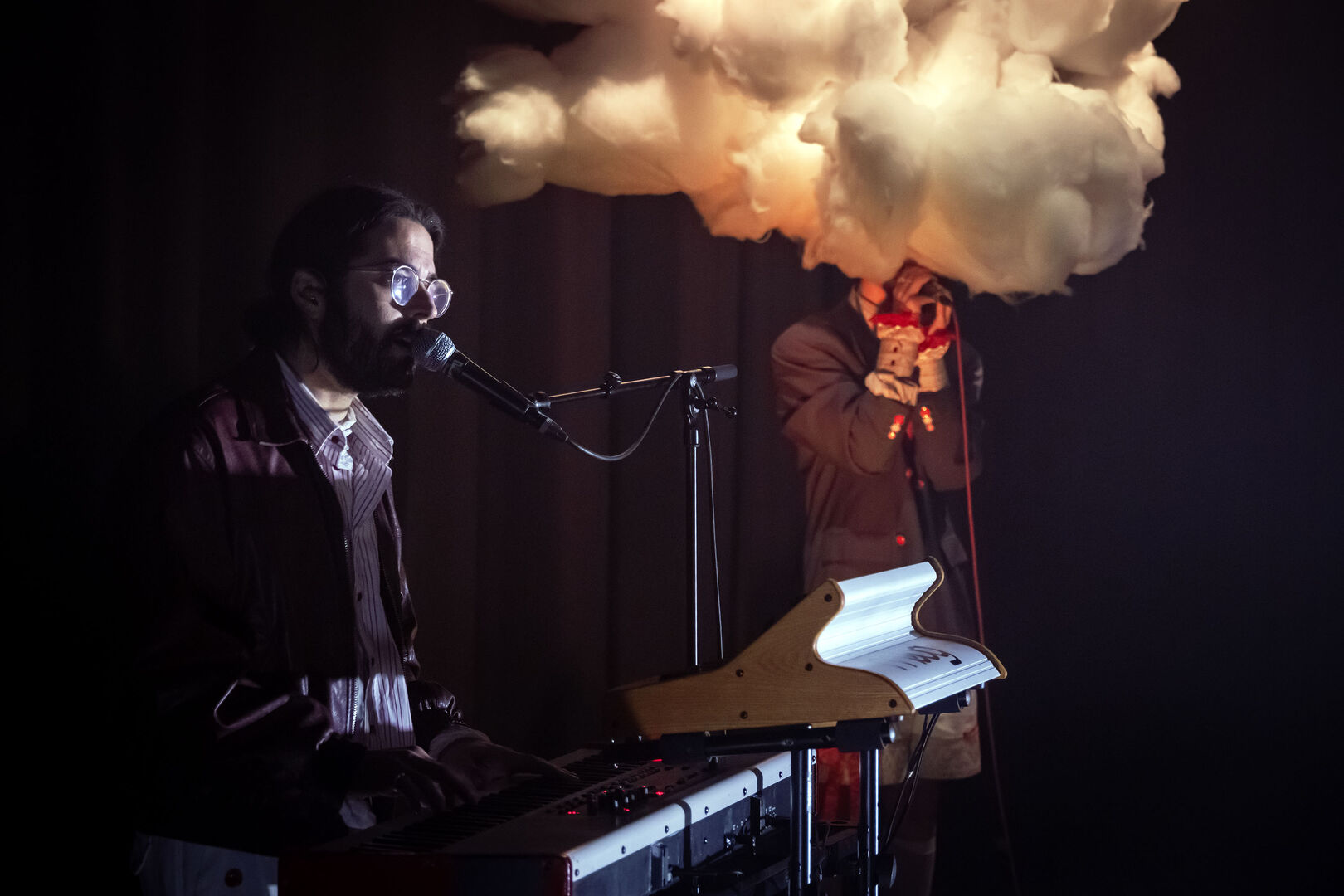 Een muzikant speelt op een keyboard terwijl een andere artiest een rookwolk uit een apparaat laat komen.