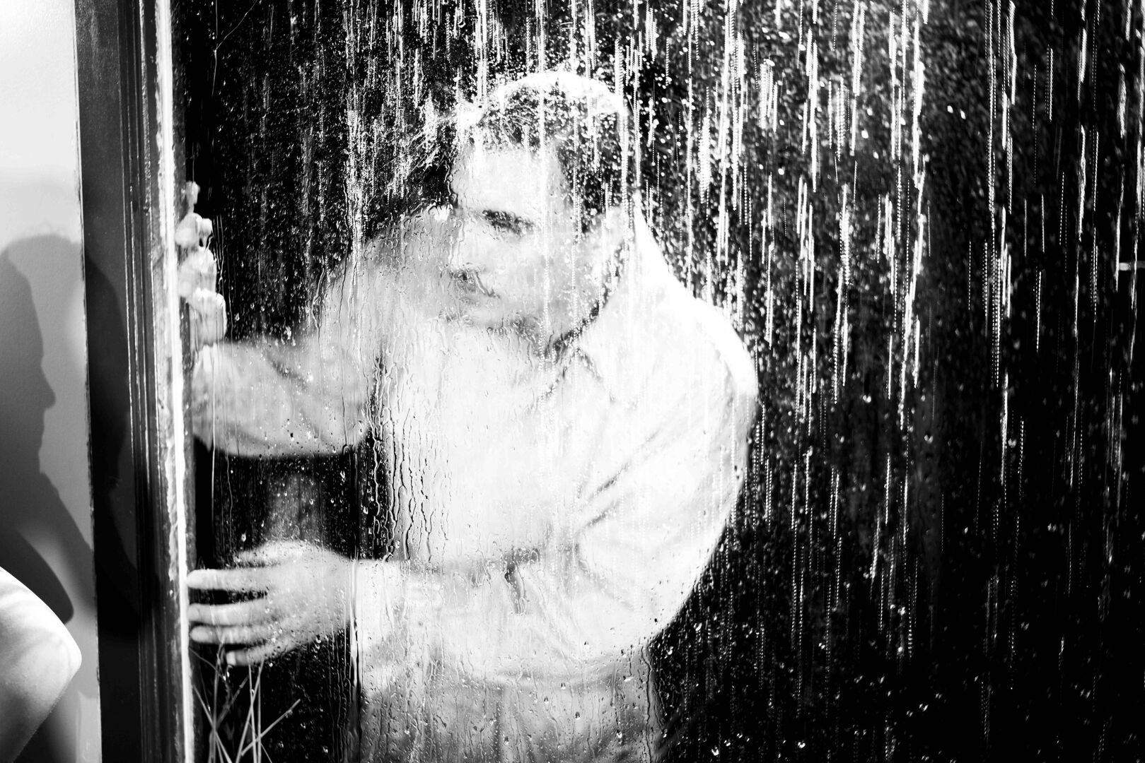 Een man in een doorweekte witte shirt staat onder een regendouche, met water dat op hem neerdaalt.