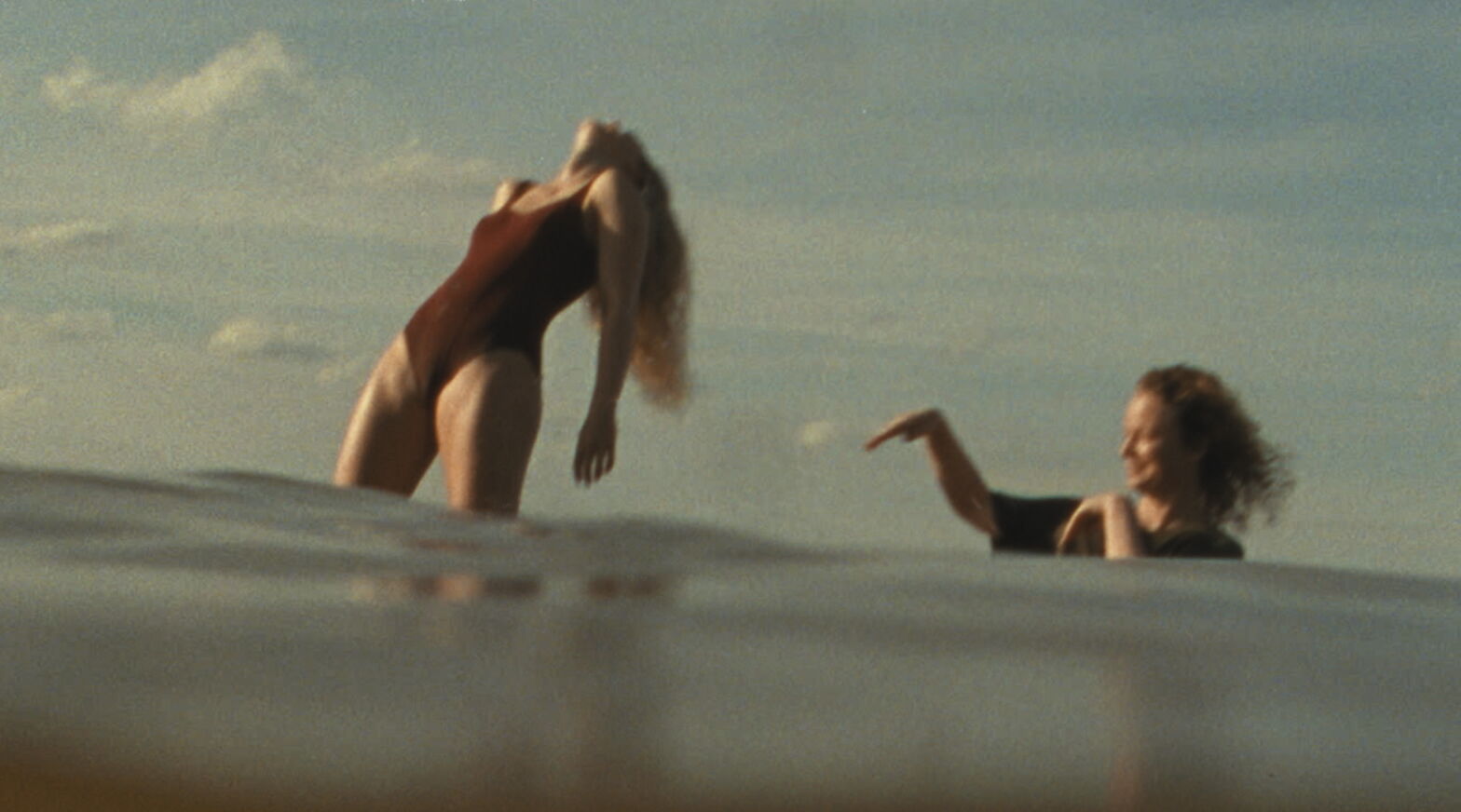 Twee vrouwen genieten van het water tijdens zonsondergang, met een speelse houding en verschijning.