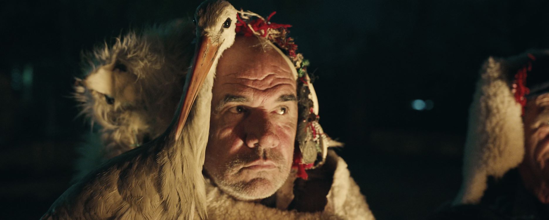 Een man met een bontkap en een serieuze uitstraling, omringd door anderen in traditionele kleding.