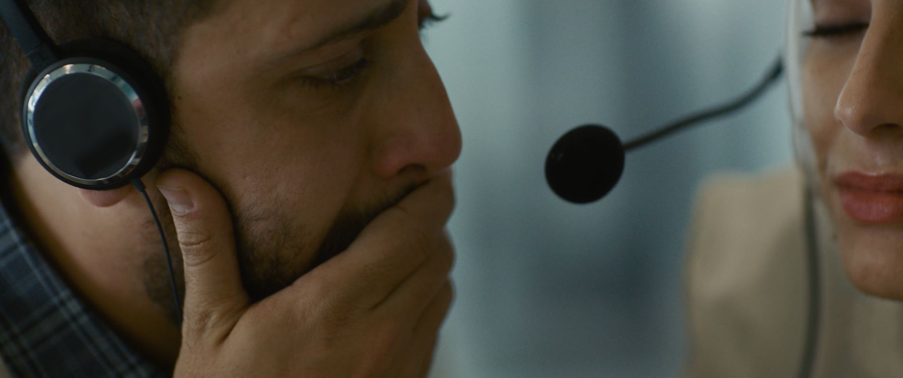 Een man en een vrouw in gesprek via een headset, de man lijkt emotioneel tijdens het gesprek.