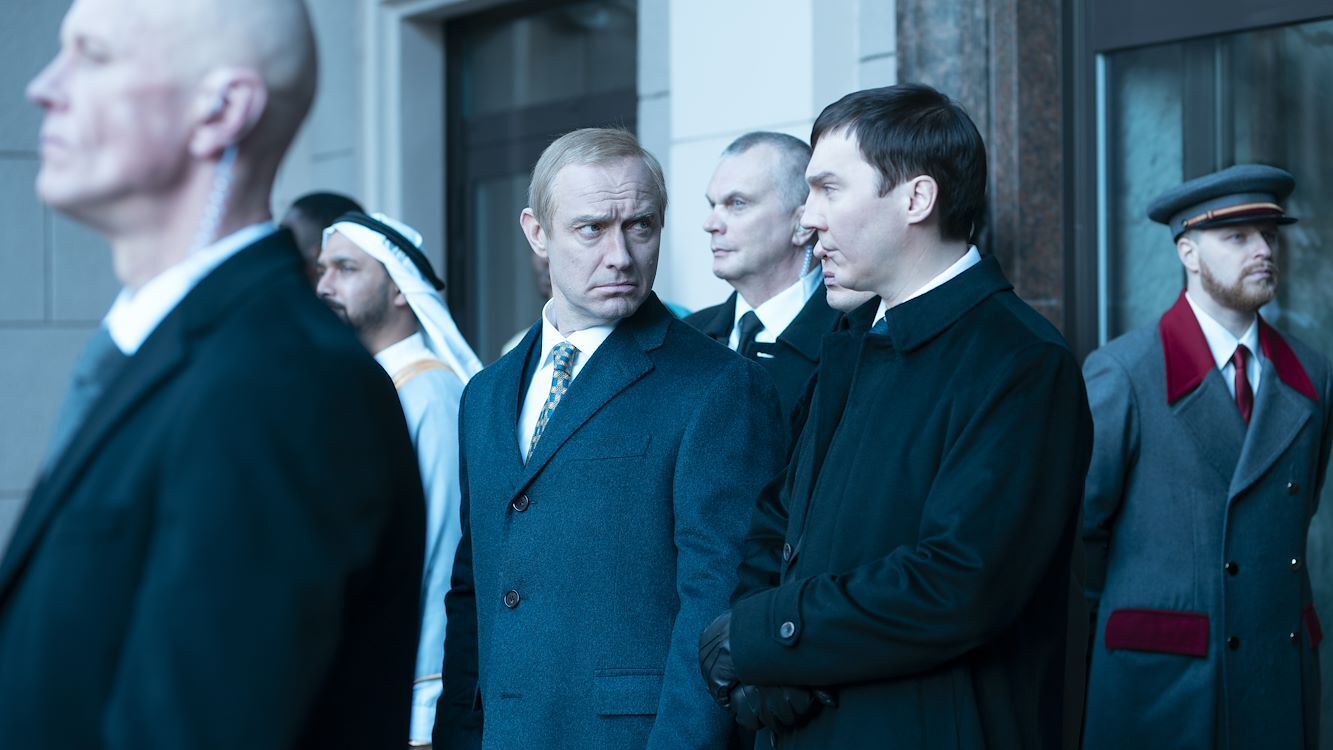 Groep mannen in formele kleding bij een evenement, met enkele in kostuums en een man in traditionele kleding.