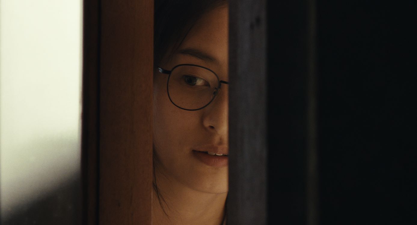 Een vrouw met een bril kijkt door een deuropening, met een gefocuste blik.
