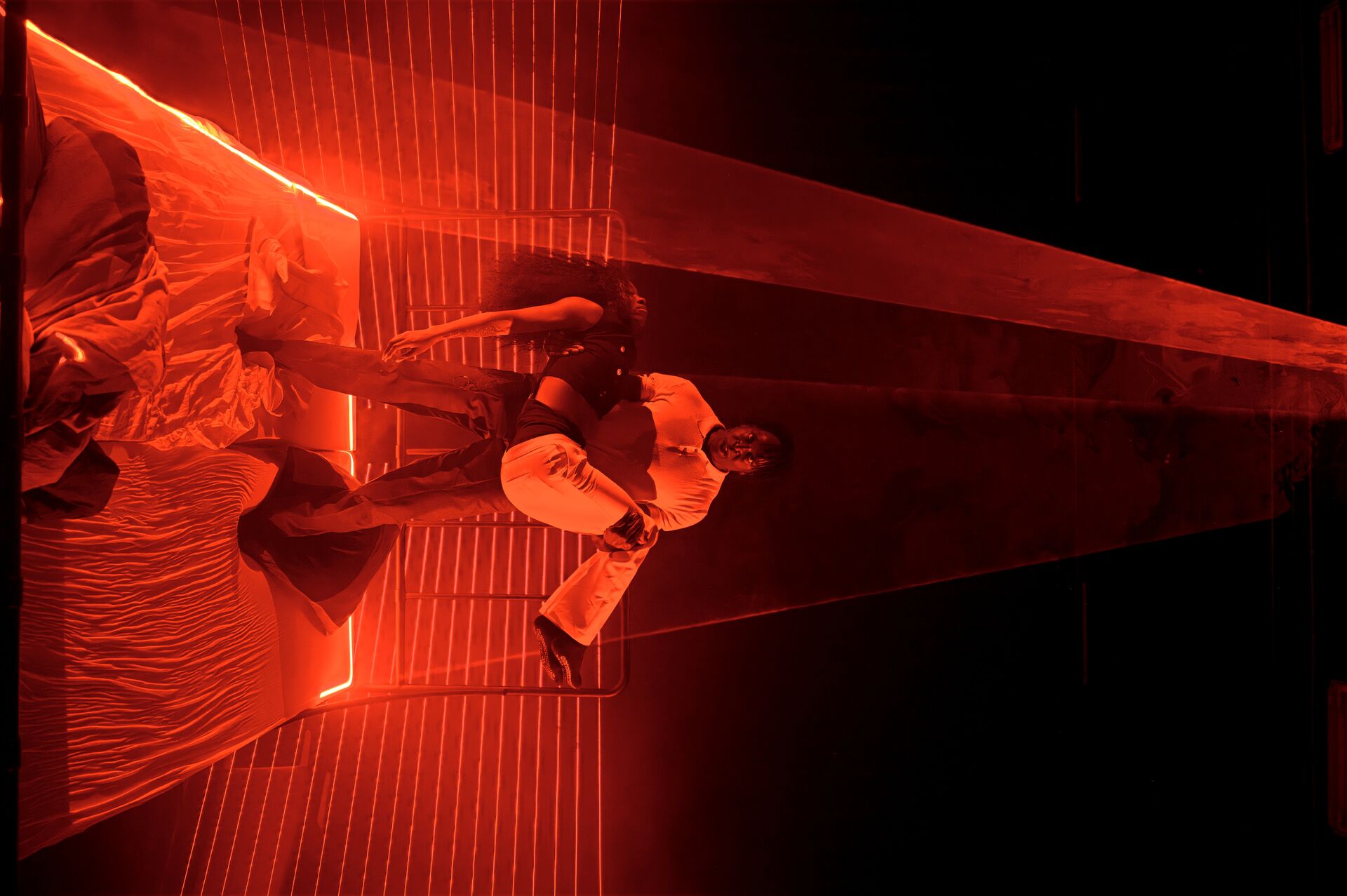 Een man tilt een vrouw op in een rood verlichte kamer met een strakke, abstracte omgeving.